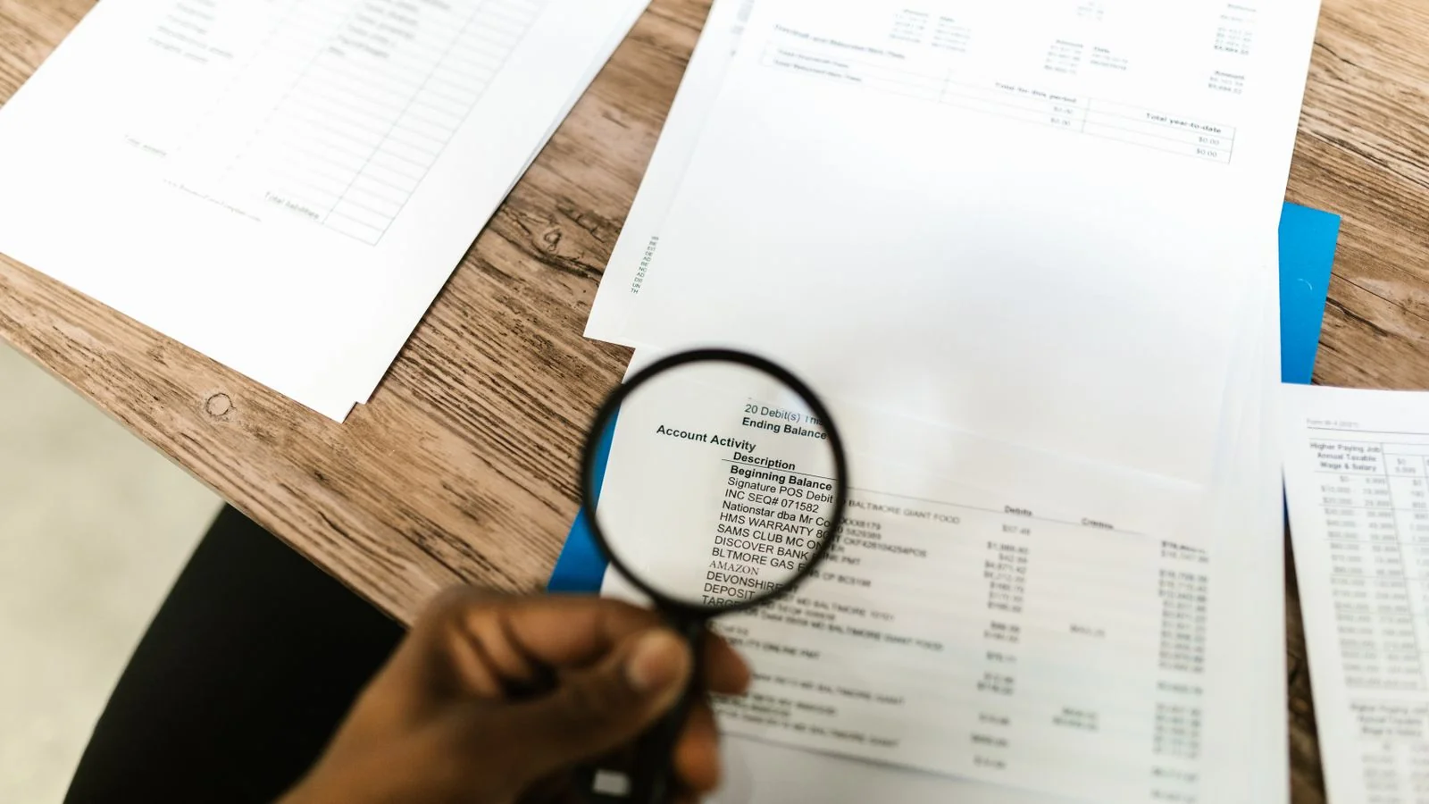 Hand holding a magnifying glass over documents, comparing details to tell entities apart