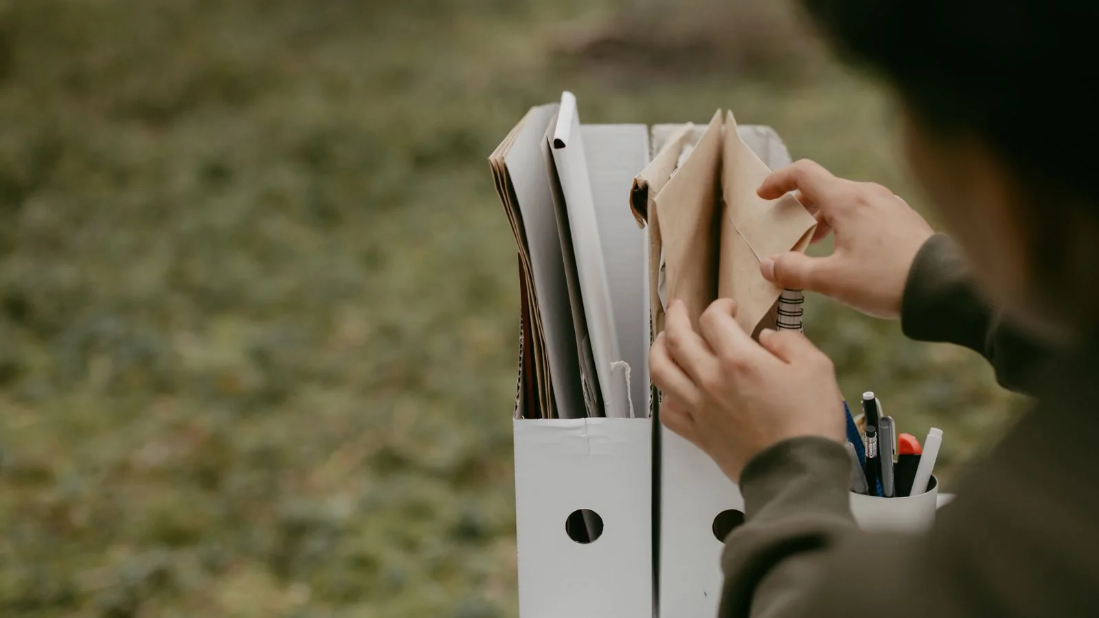 Hands sorting printed documents into labeled folders outdoors, like organizing schema data