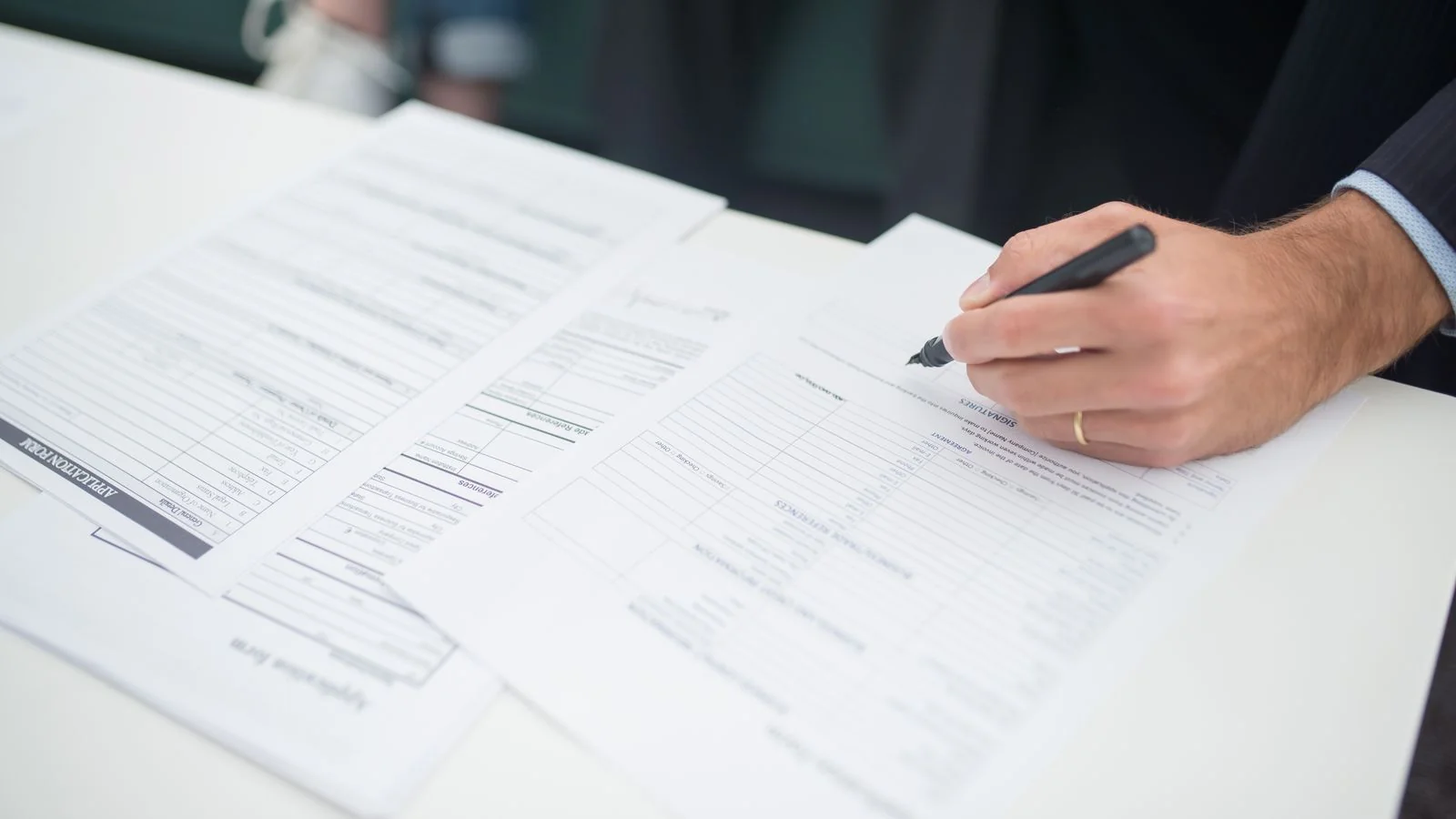 Hand signing business documents at a desk, the paperwork behind every new business application