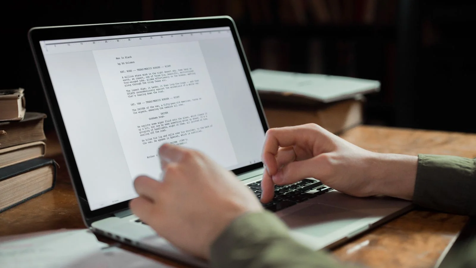 A person typing on a laptop surrounded by books, the steady volume one writer alone cannot sustain