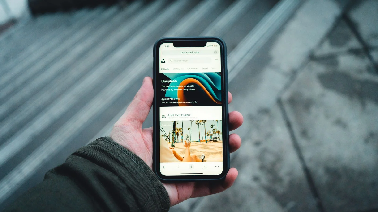 Hand holding a smartphone open to a search page on a city street