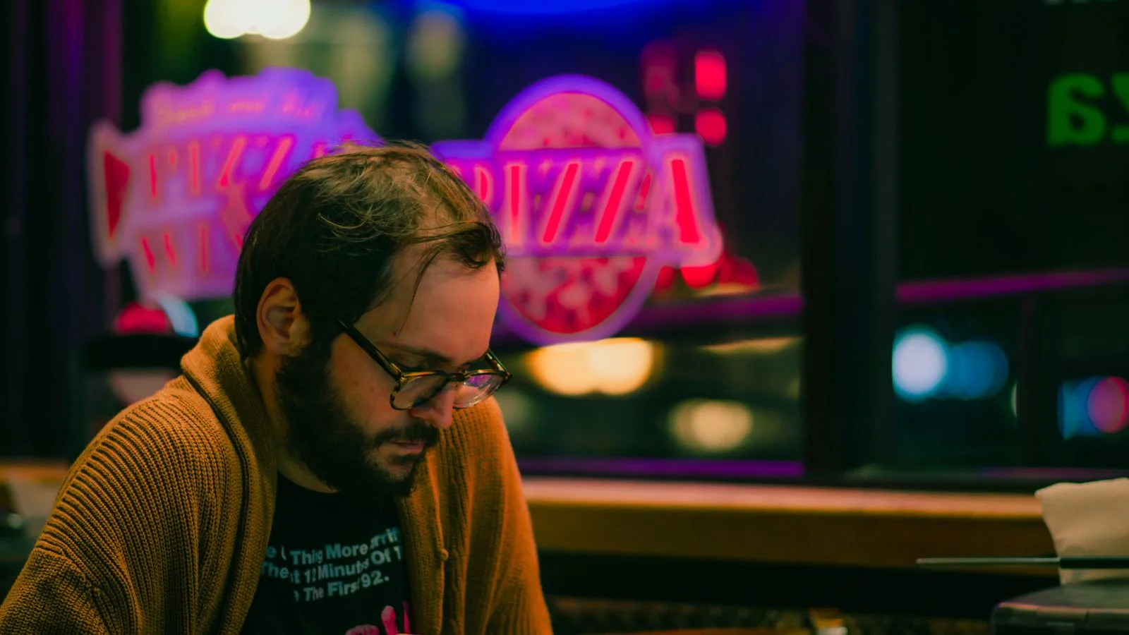 A diner relaxing in a neon-lit pizzeria, the customer a panel sends through the door