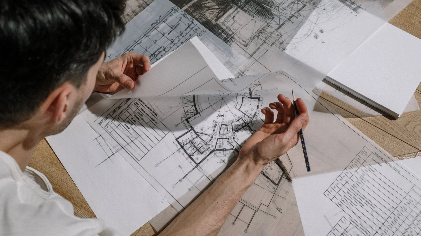 Architect studying and sketching over detailed blueprints at a desk