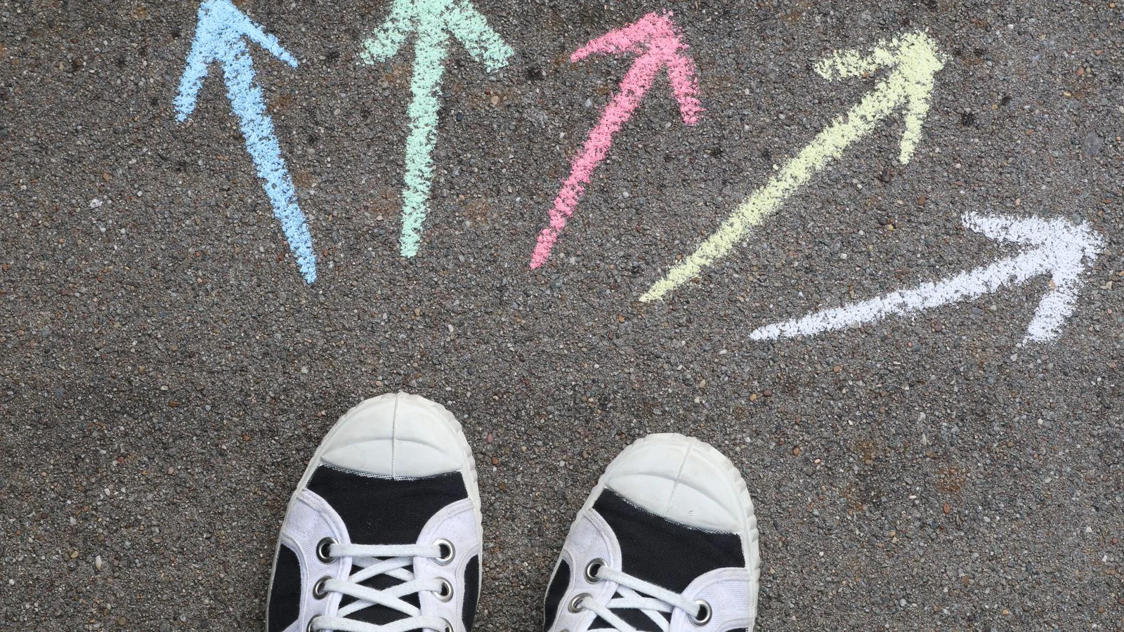 Black sneakers beside chalk arrows pointing in different directions on pavement