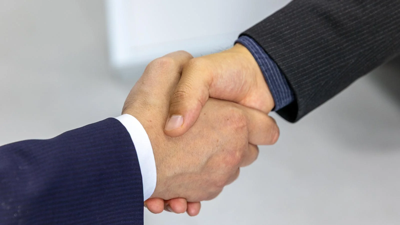 Two professionals shaking hands across a meeting table in a brightly lit office