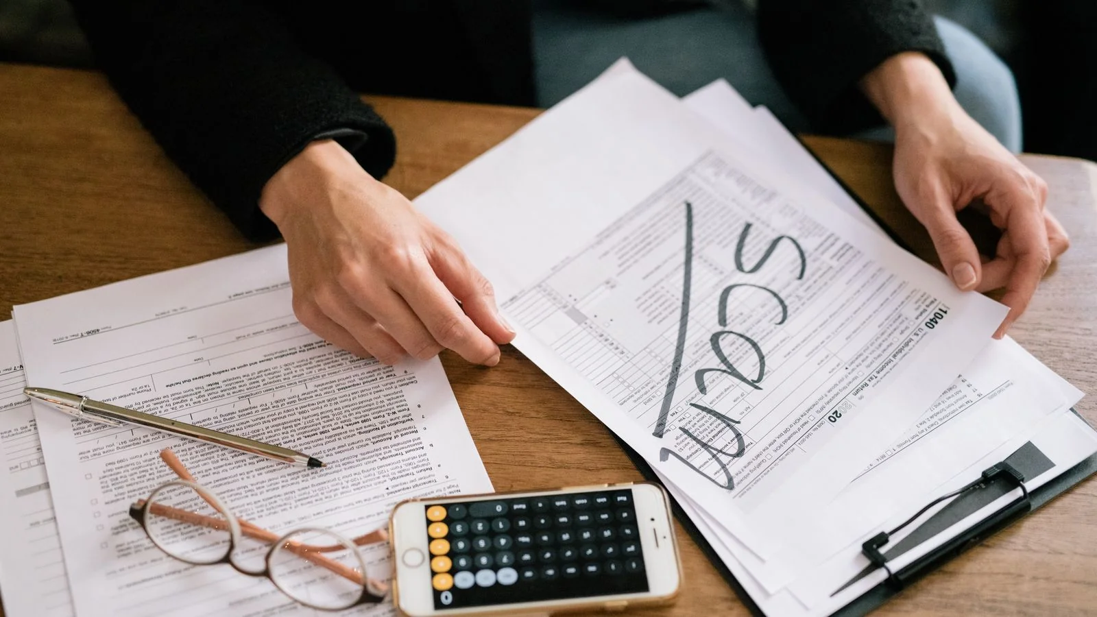 Hands examining printed forms with a calculator, the kind of verification work that mirrors how Google vets a source