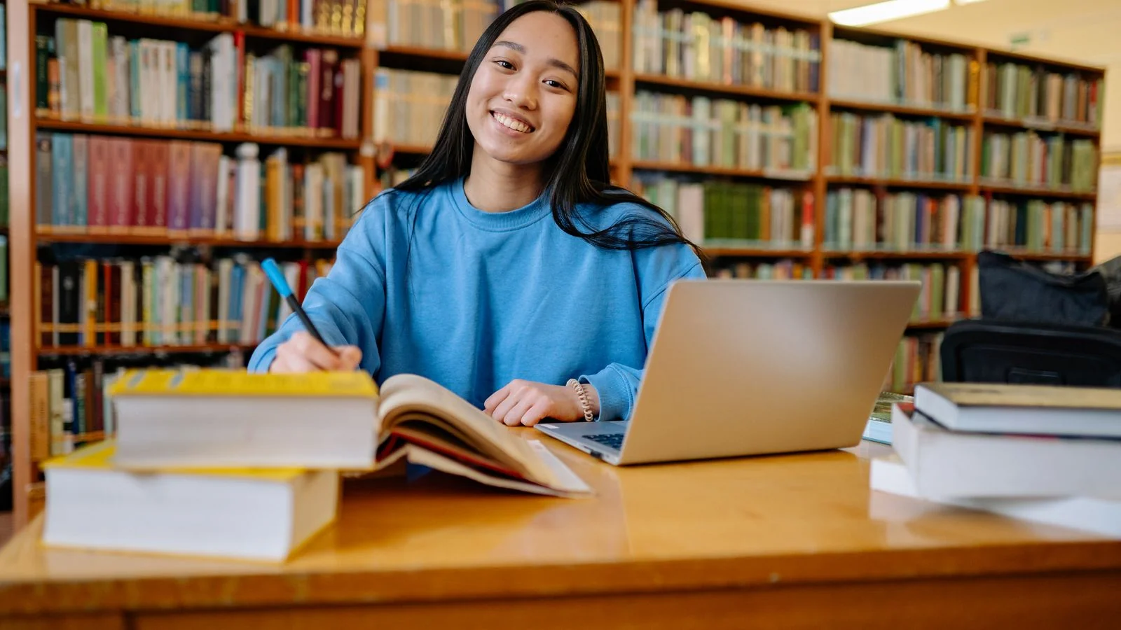 A student studying with books and a laptop in a library, the research posture Perplexity imitates at speed