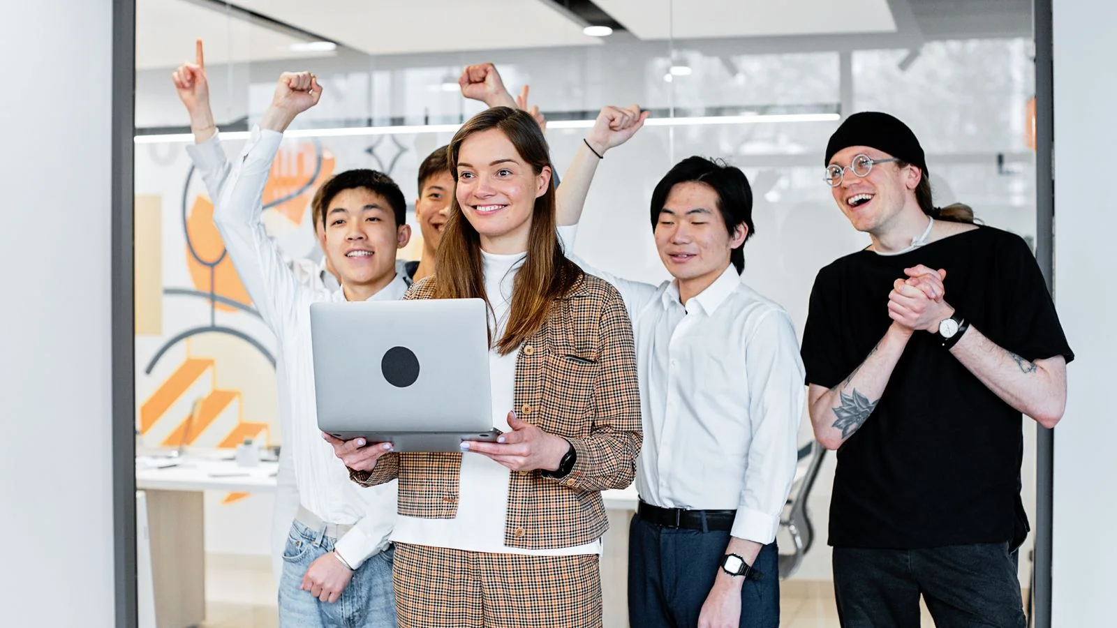 Colleagues gathered around a laptop in an office, smiling and pointing at the screen as they review something together