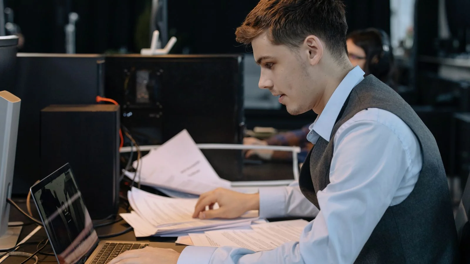 Young professional working through documents beside a laptop at an office desk, the manual research a real media list requires