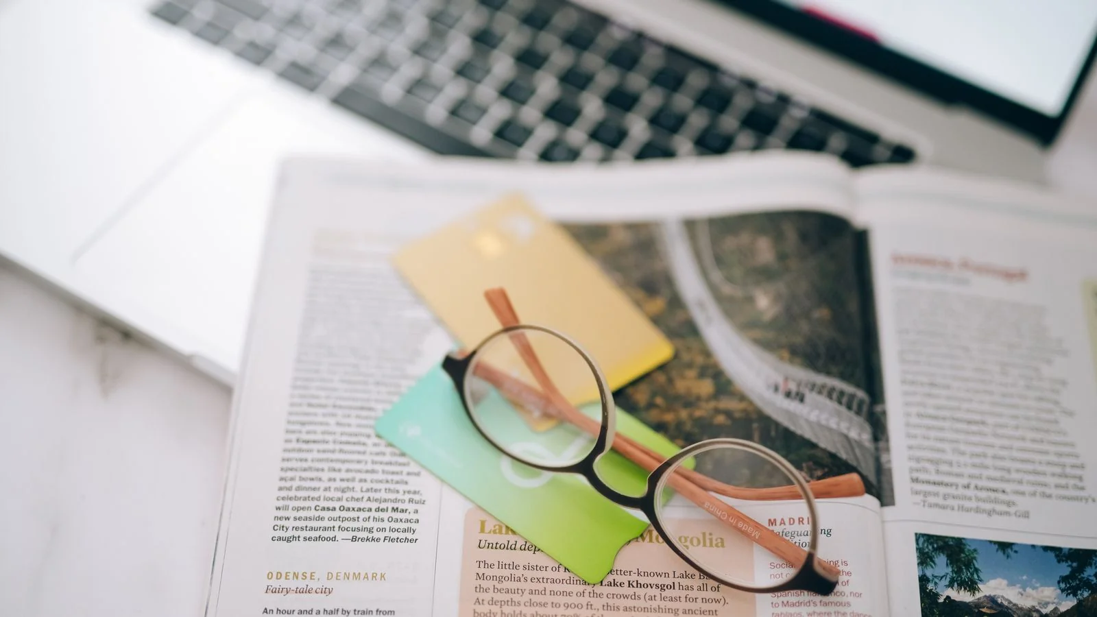 Reading glasses, index cards, and a magazine spread out near a laptop, the sourcing pass that fills a media list