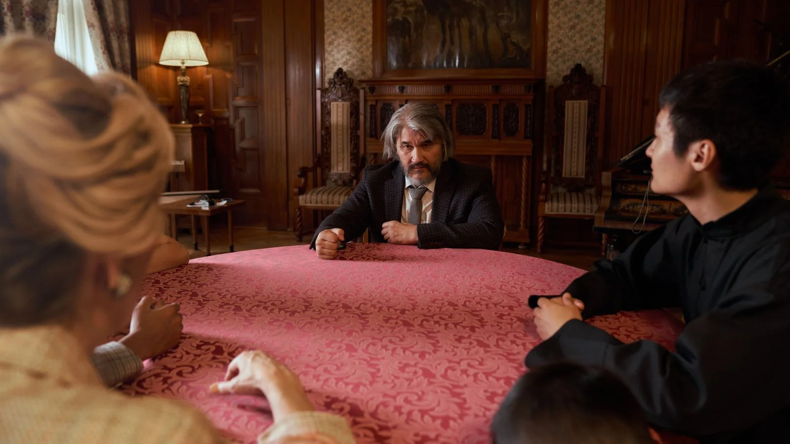 A group seated around a round table in a vintage room, engaged in formal discussion