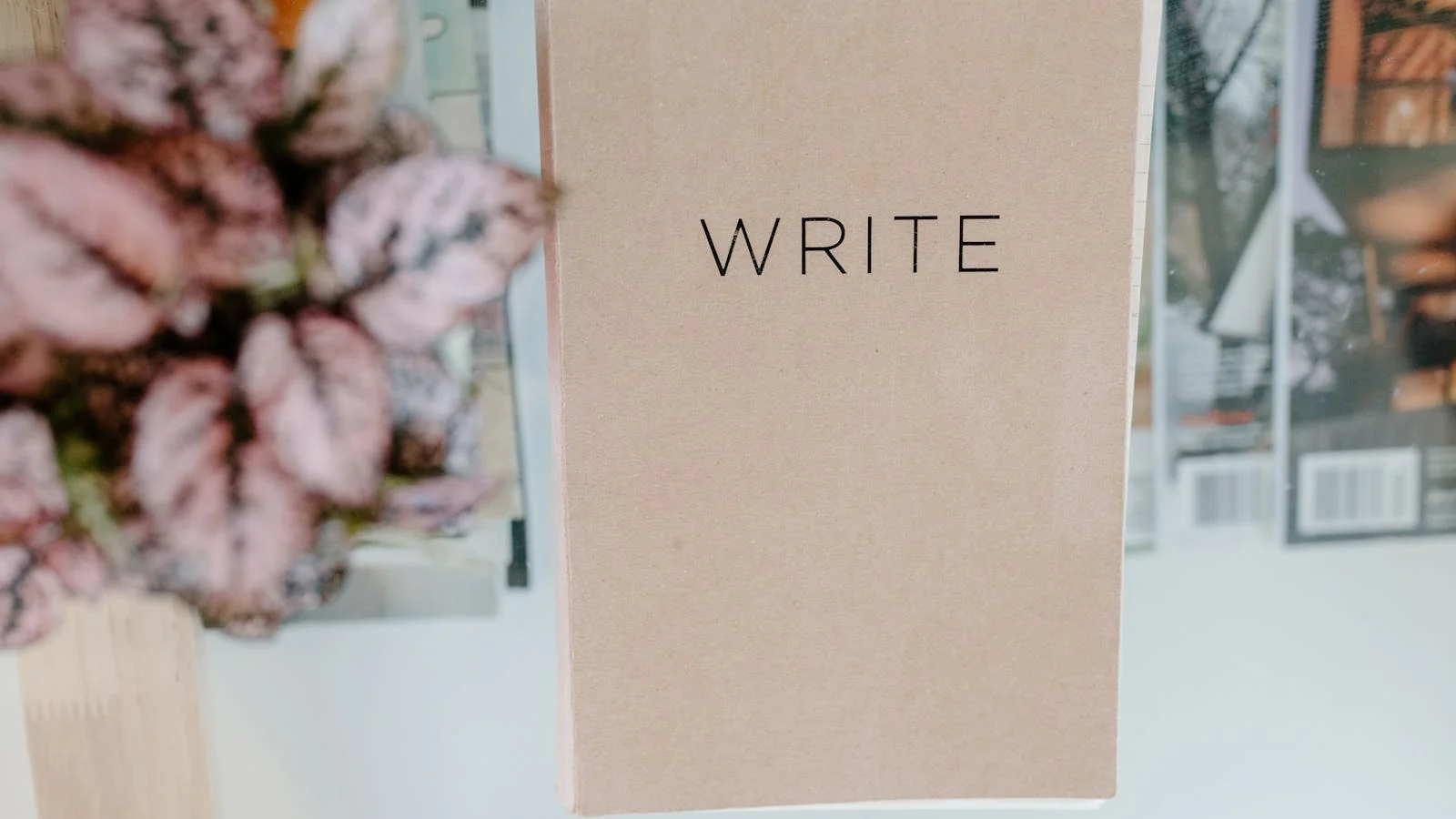 A notebook with the word WRITE on the cover sits on a glass table beside magazines