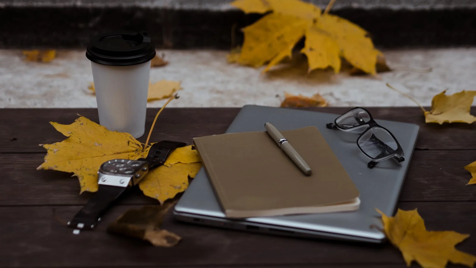 A notebook, pen, and eyeglasses resting on a laptop on a desk