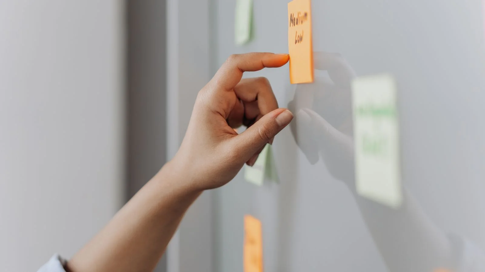 Hand placing a sticky note onto a reflective office surface, ordering questions into a sequence before any writing starts