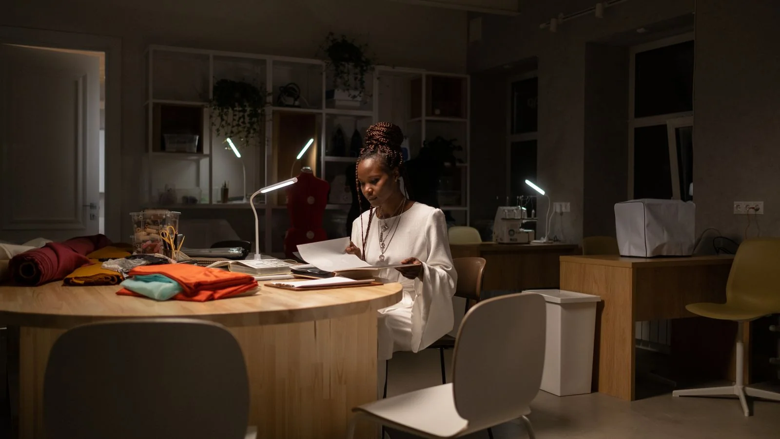 Designer working alone under studio lights at night, the quiet output that separates authority from visibility