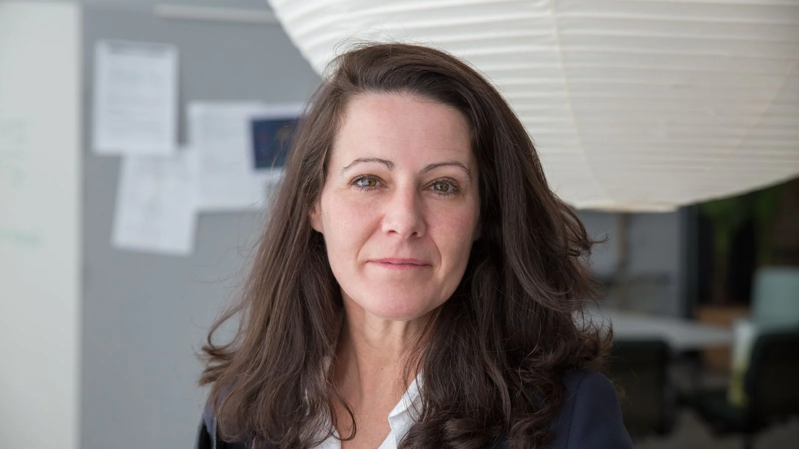 A thoughtful businesswoman in a blazer reviewing notes at a desk in a bright office