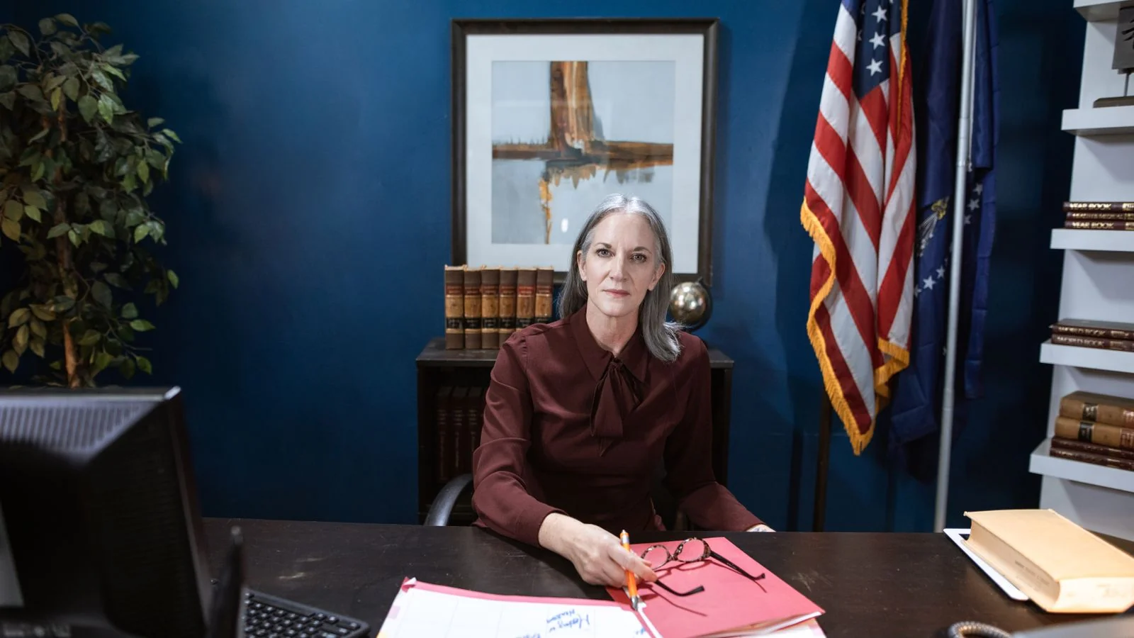 A professional woman seated at a wooden table in an office, representing authority and leadership