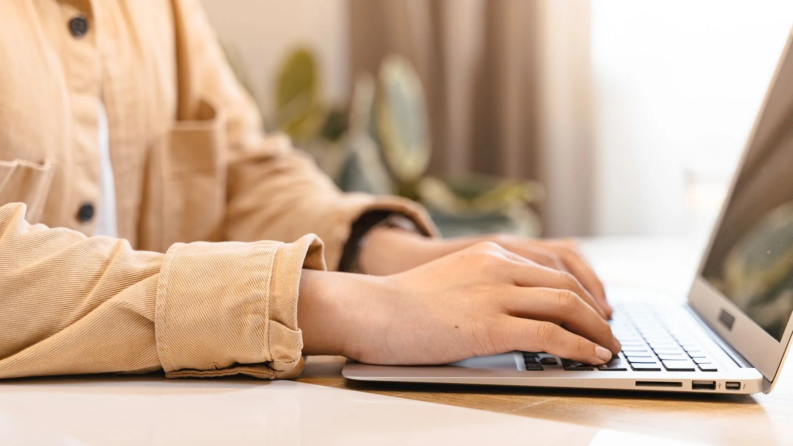 Close-up of hands typing on a laptop, drafting content at a desk