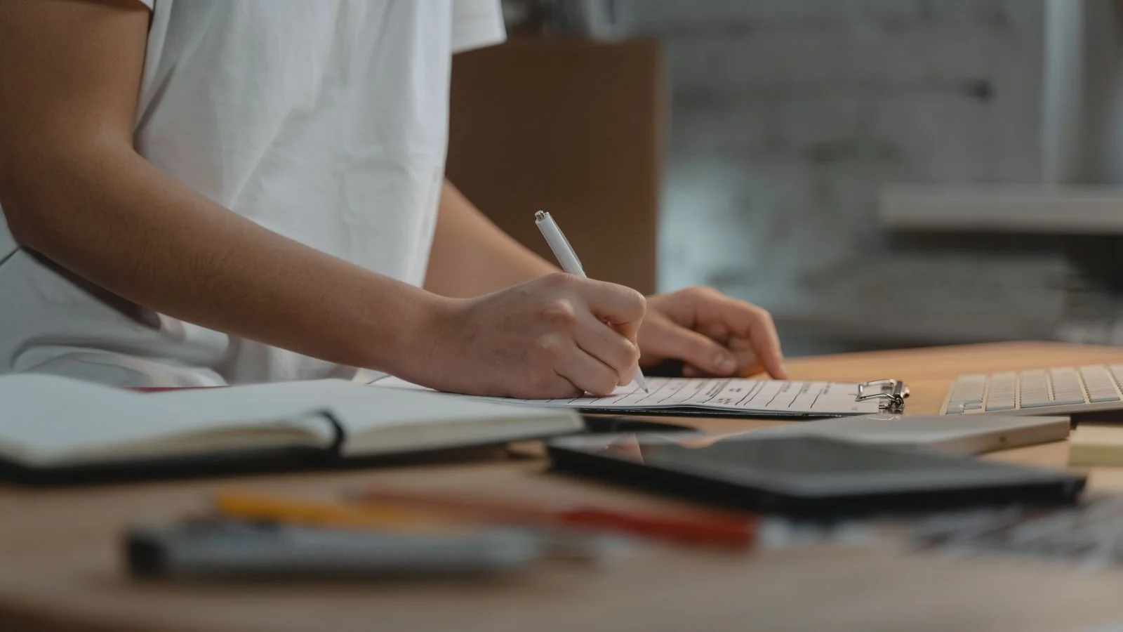 A person writing notes on a clipboard at a desk with office supplies