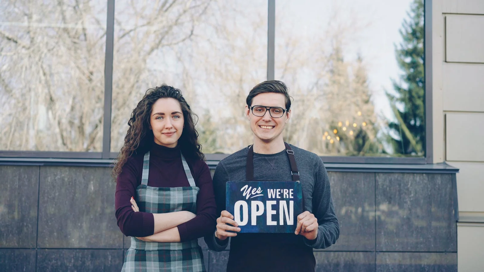 Two small business owners standing outside their shop holding an open sign