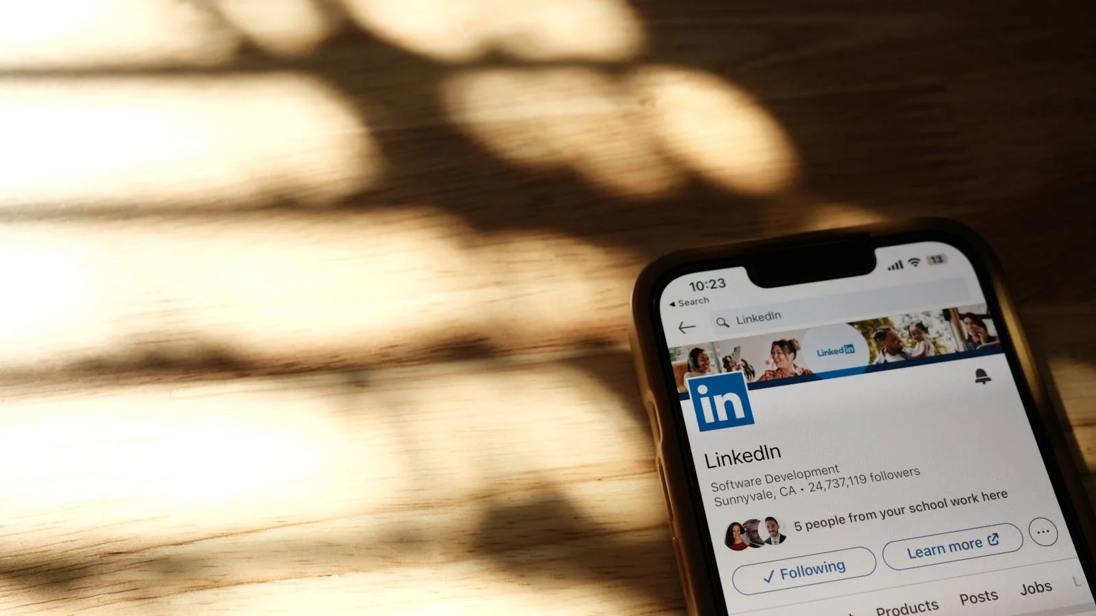 A LinkedIn page displayed on a phone resting on a wooden desk in daylight