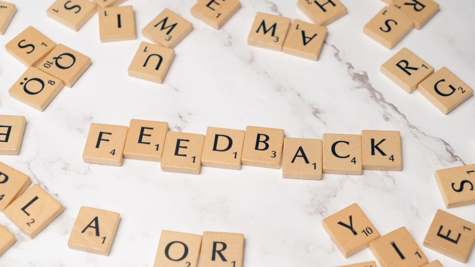 Wooden Scrabble tiles spelling feedback on a marble surface