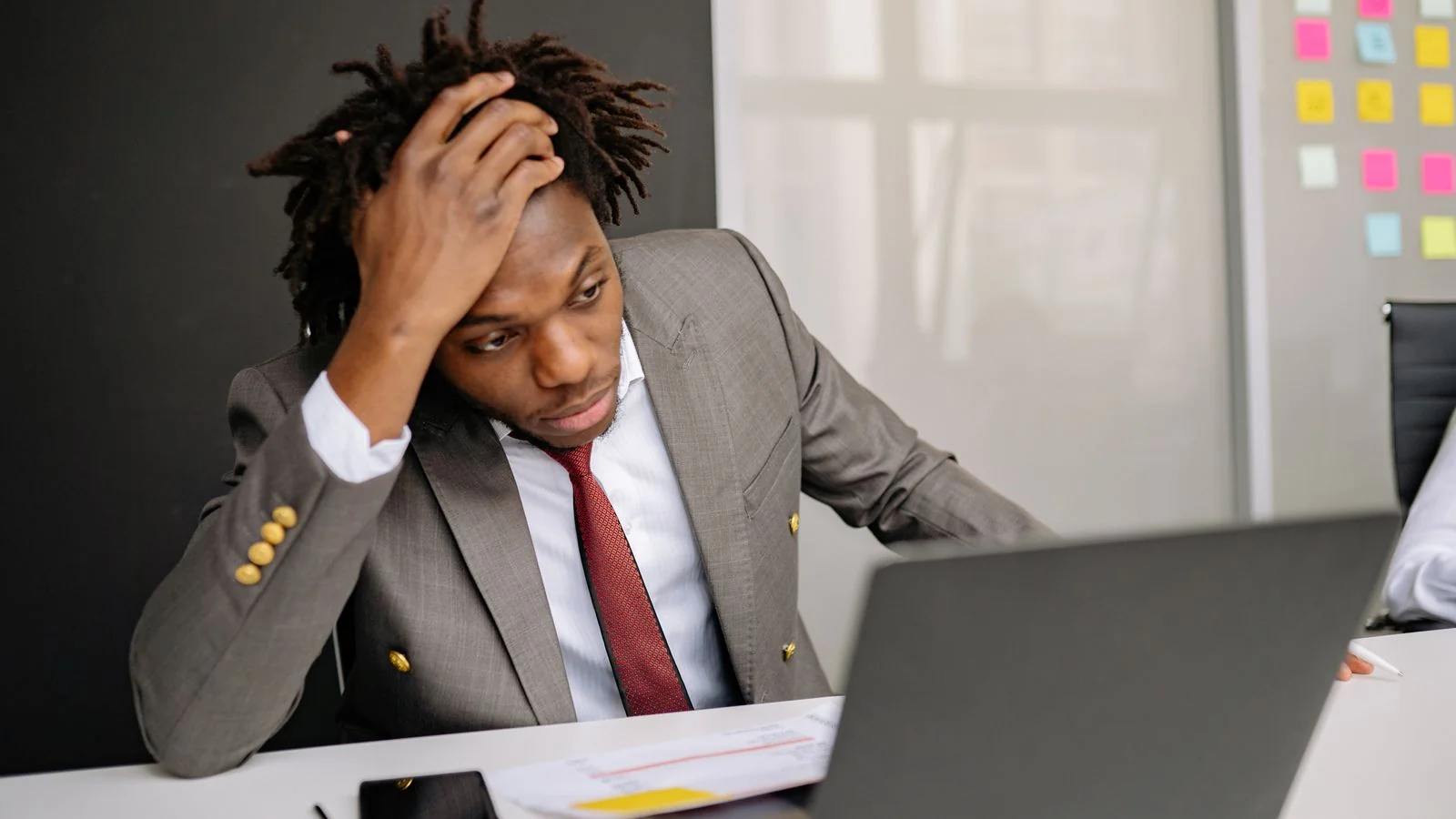 A worried businessman working on a laptop in an office, reviewing something on screen