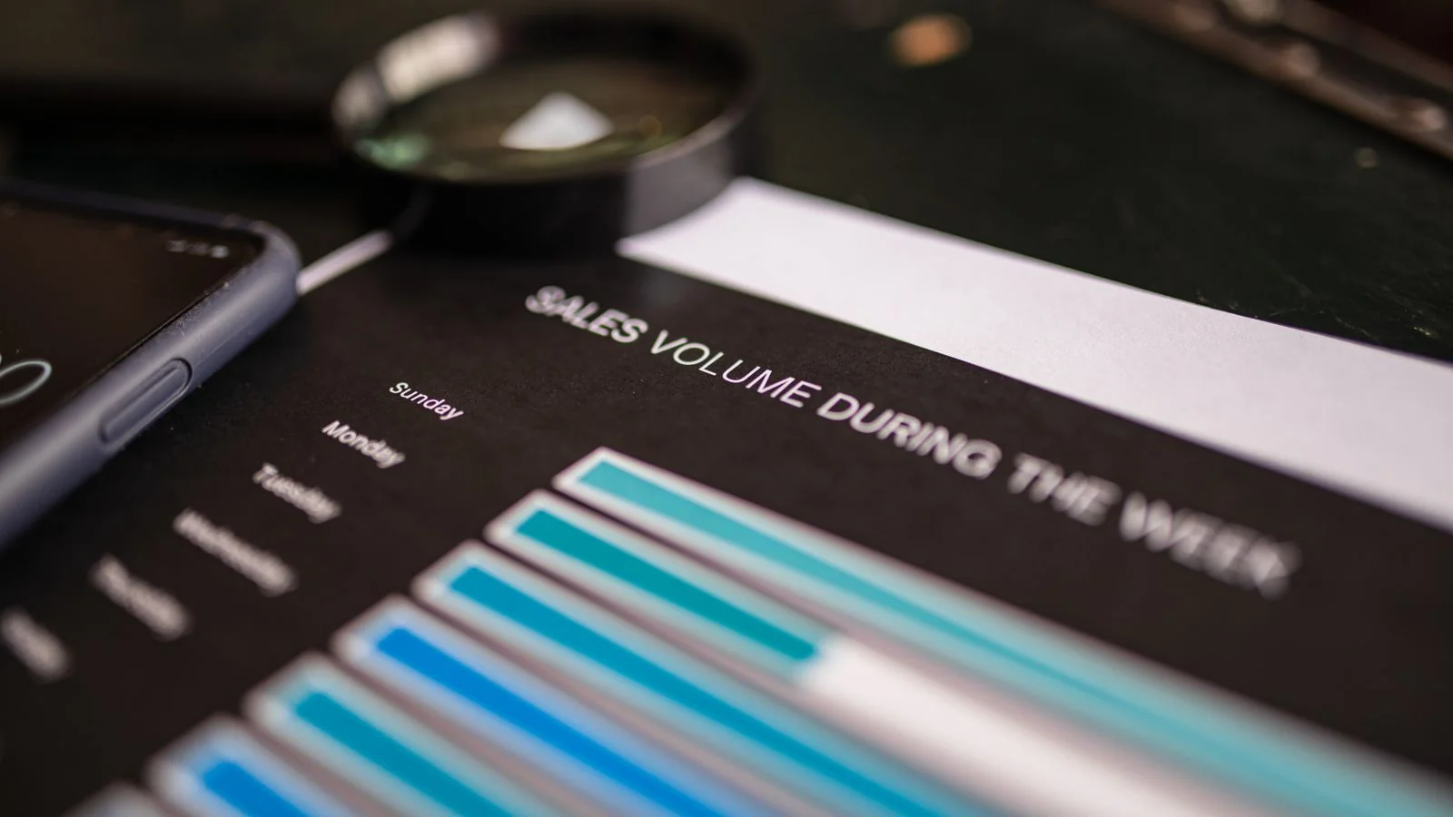 Magnifying glass resting on a printed volume chart next to a phone, the close inspection a GEO audit demands