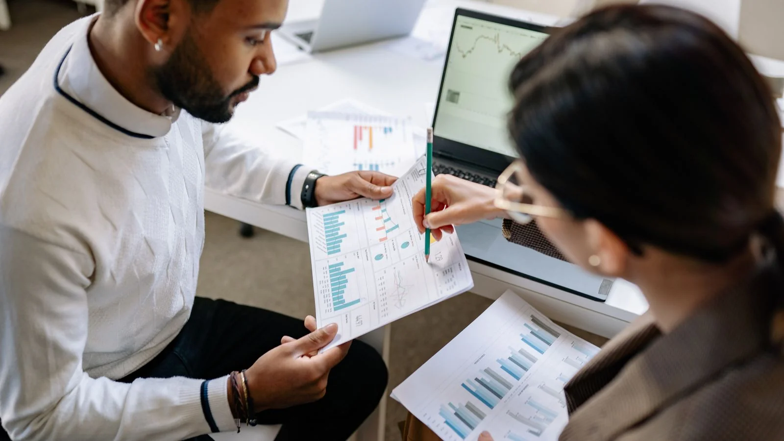 Two colleagues comparing printed graphs and on-screen data, the kind of side-by-side review the Answer Ledger enables
