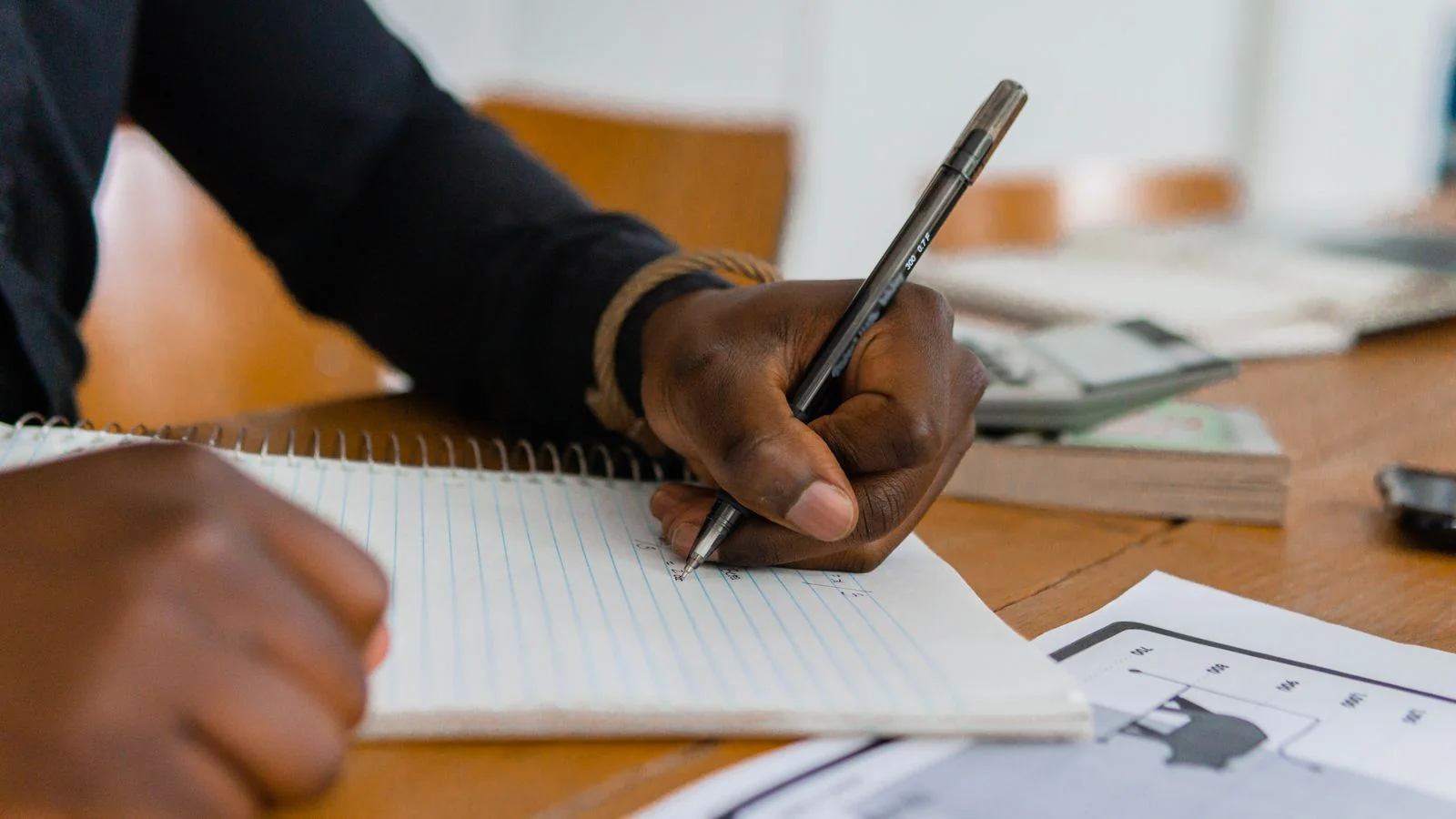 A person writing in a notebook beside research notes, building the data that earns press links