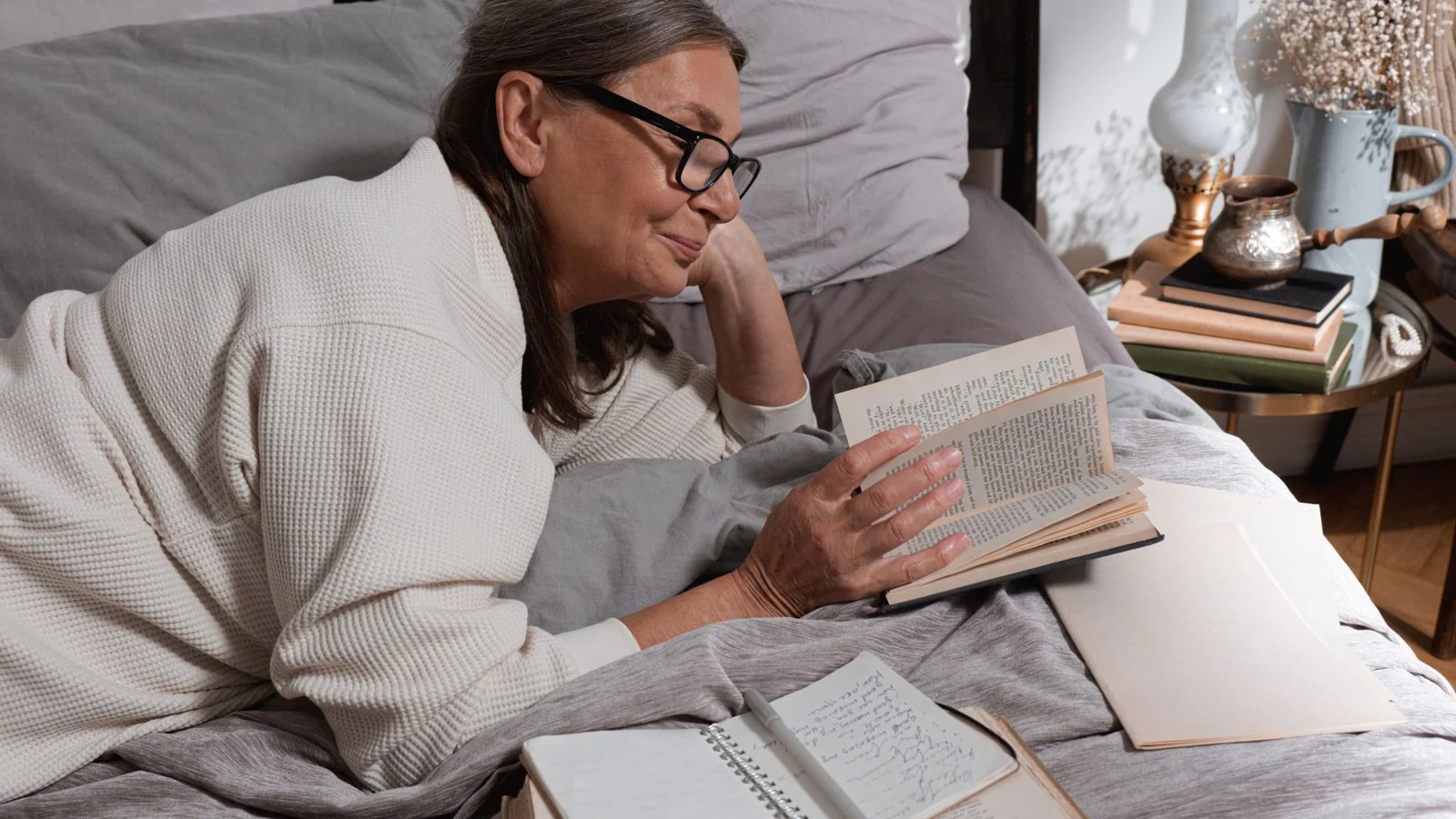 Senior woman with glasses reading comfortably in bed under a blanket