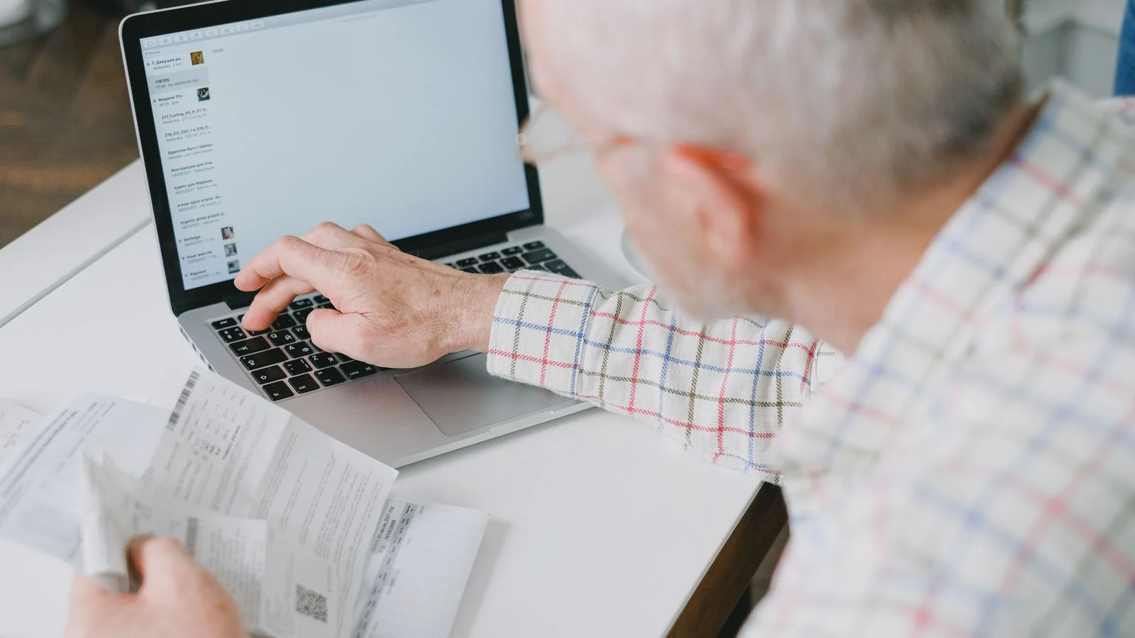Older man at a desk working through documents and a laptop, managing household finances