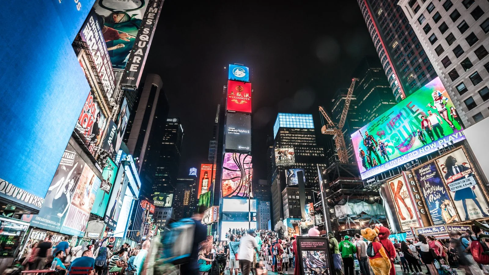 Times Square billboards glowing at night above crowds in New York City