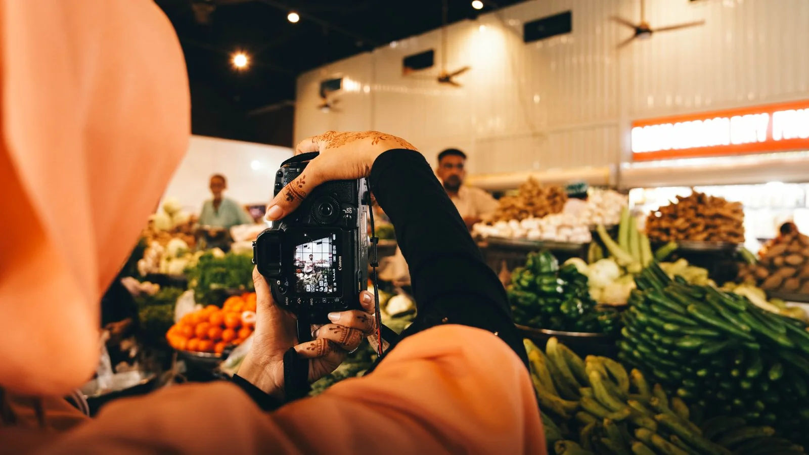A woman photographer with henna on her hands shooting vegetables at an indoor market in Sindh, Pakistan