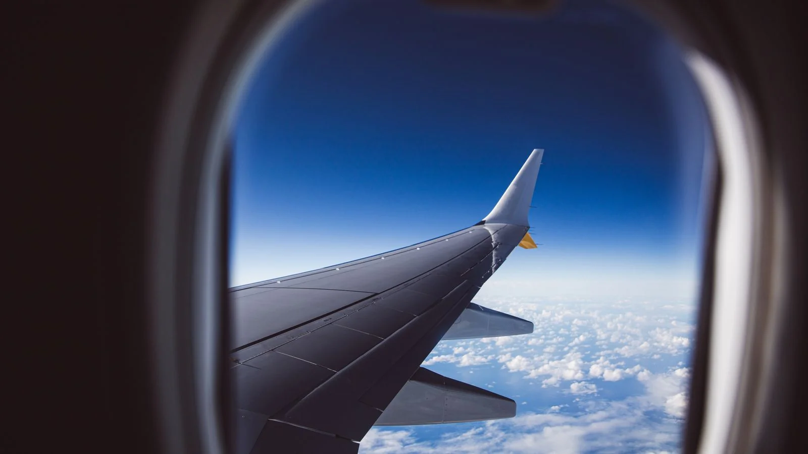 View from an airplane window of the wing over a layer of white clouds in daylight