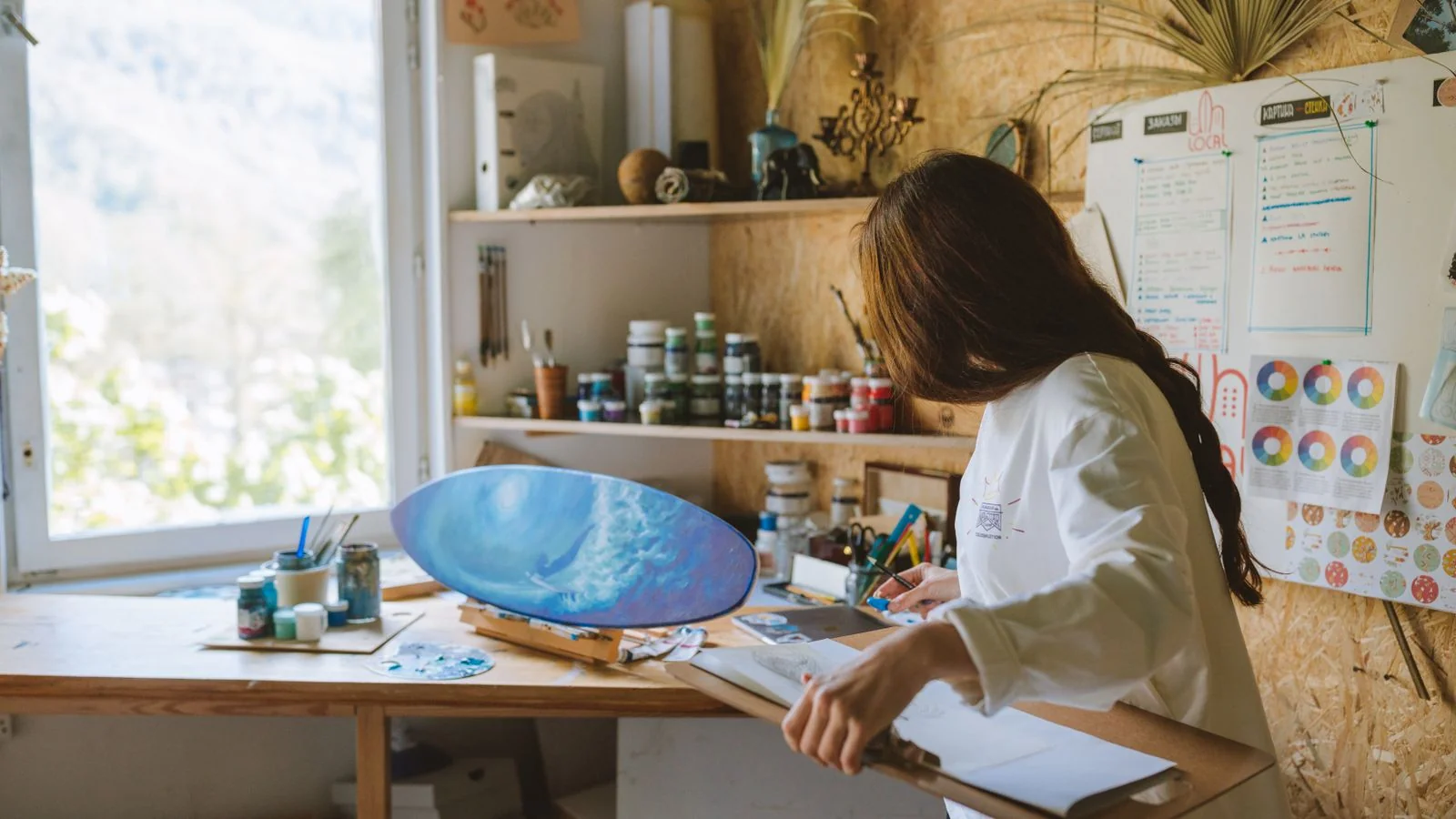 Painter working on a canvas in a sunlit studio crowded with supplies