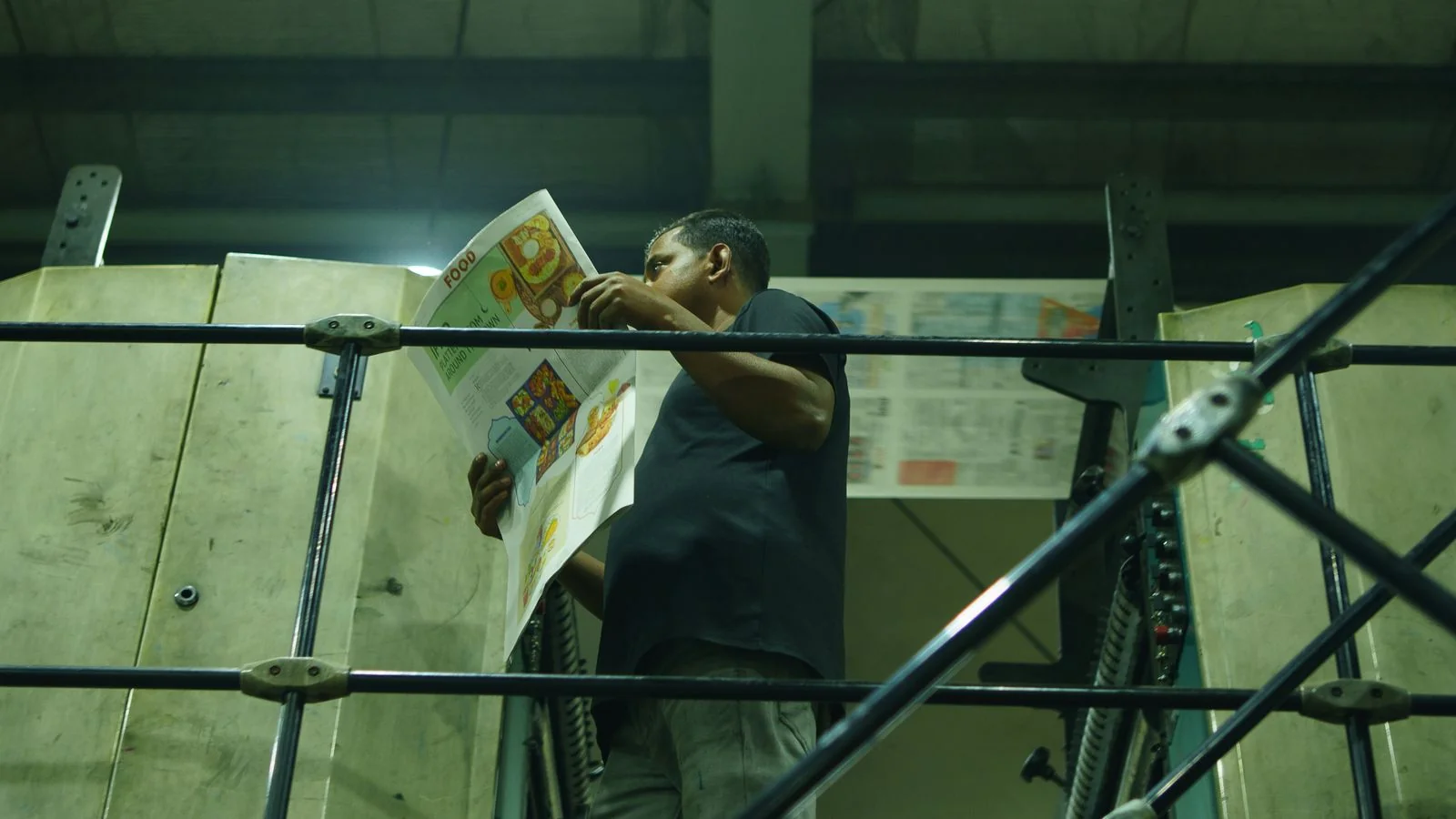 Pressman inspecting fresh newspapers coming off an industrial printing line