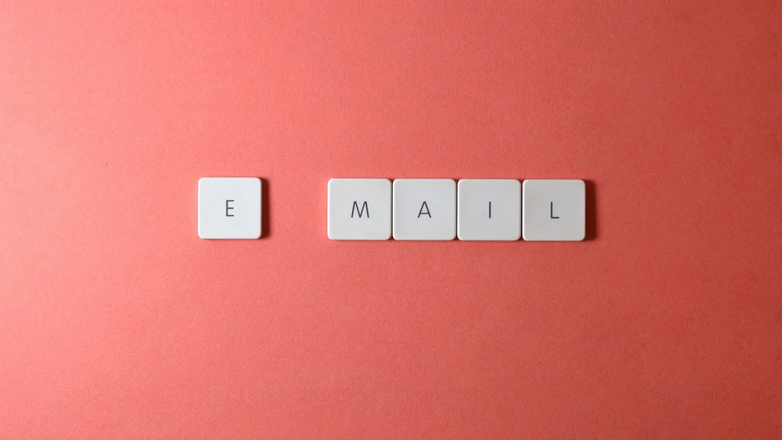Coral-pink keyboard tiles spelling 'email' in a tight overhead frame, the visual reminder that every BI pitch lives or dies as a subject line
