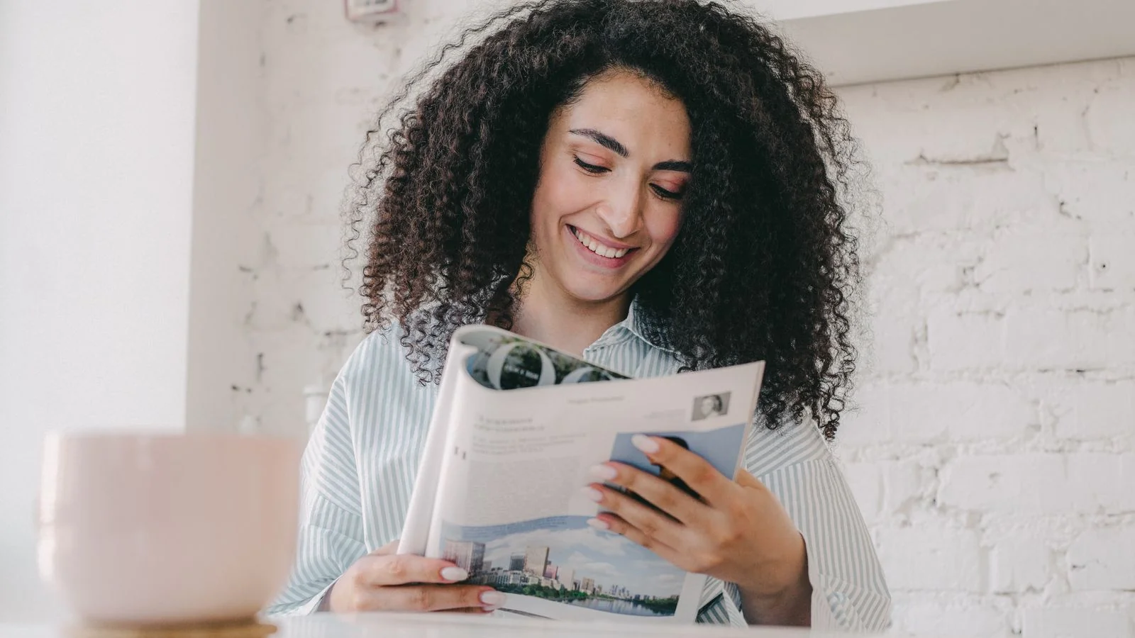 A woman reads a magazine at home with a ceramic mug beside her