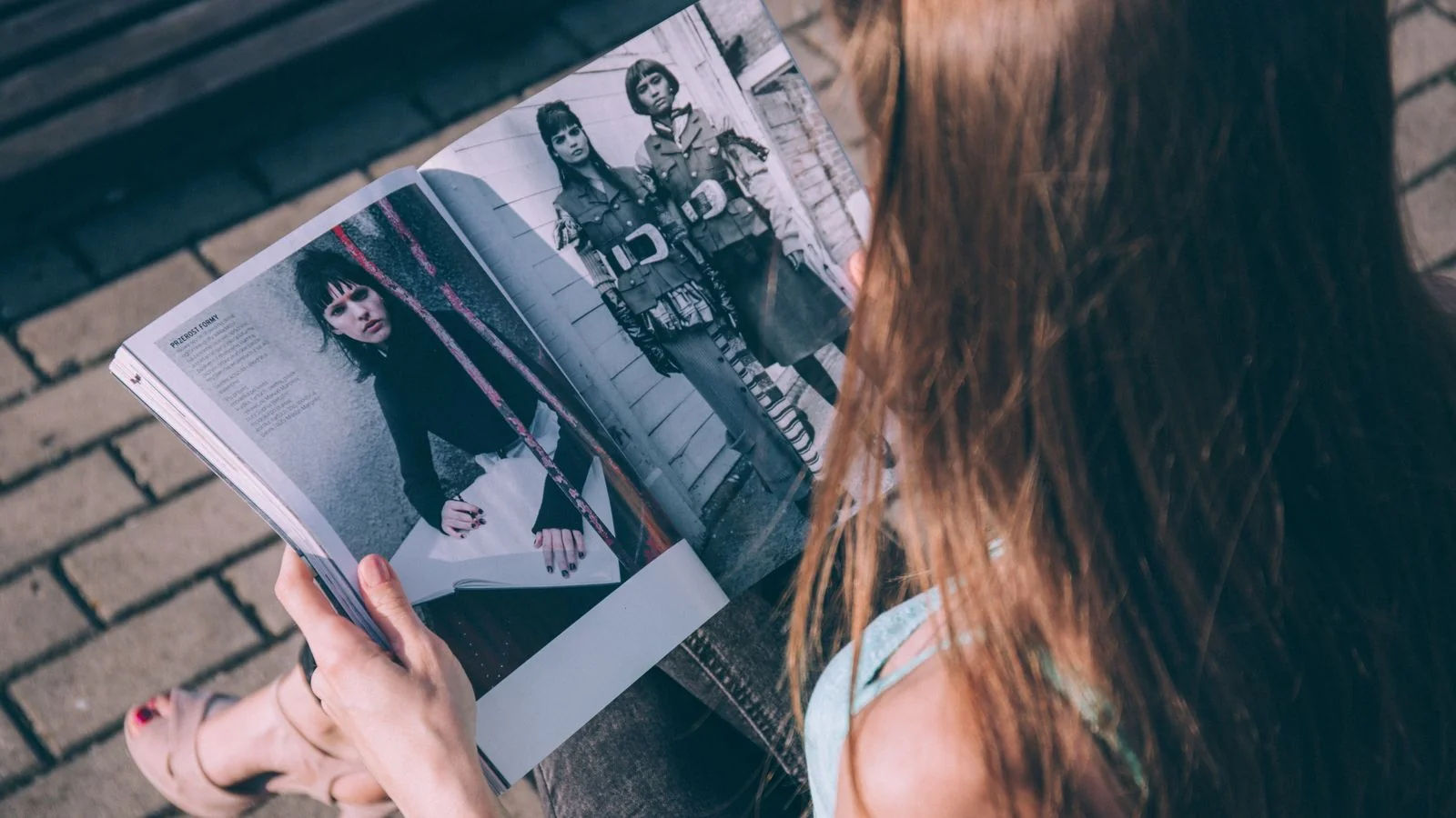 A woman reading a fashion magazine outdoors, focused on the pages