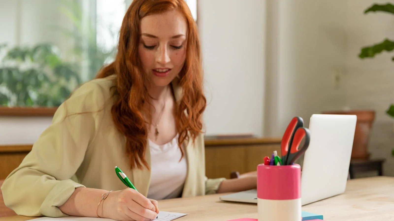 Woman writing at a home office desk beside a laptop, drafting the 600-word op-ed Crain's asks for