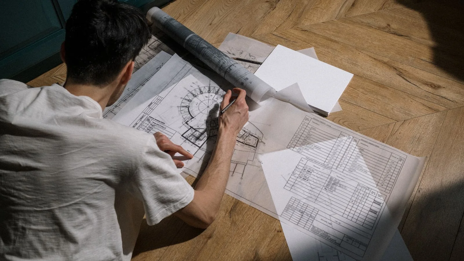A man drawing architectural designs on a wooden floor in daylight, the kind of project origin story Dwell editors want in a pitch