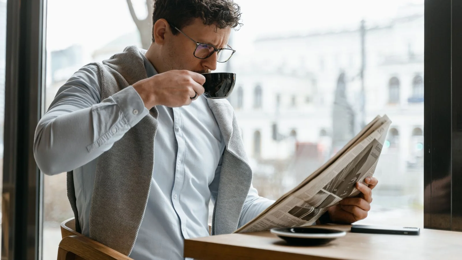 Reader working through a newspaper over coffee in a quiet cafe