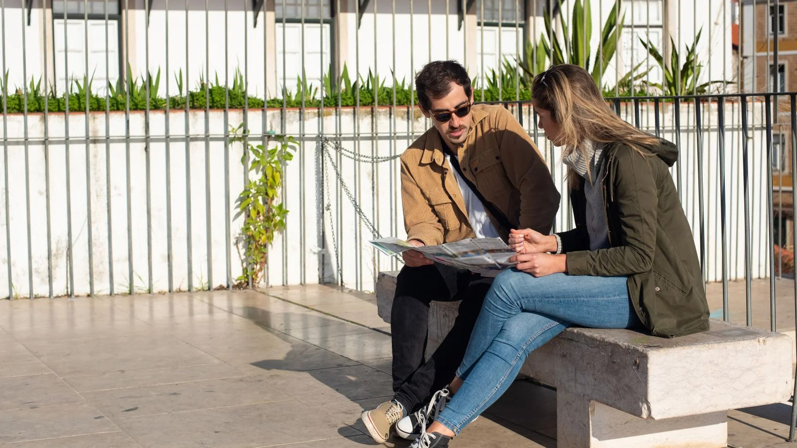 Two tourists on a sunny bench studying a paper map, planning their route through a new destination