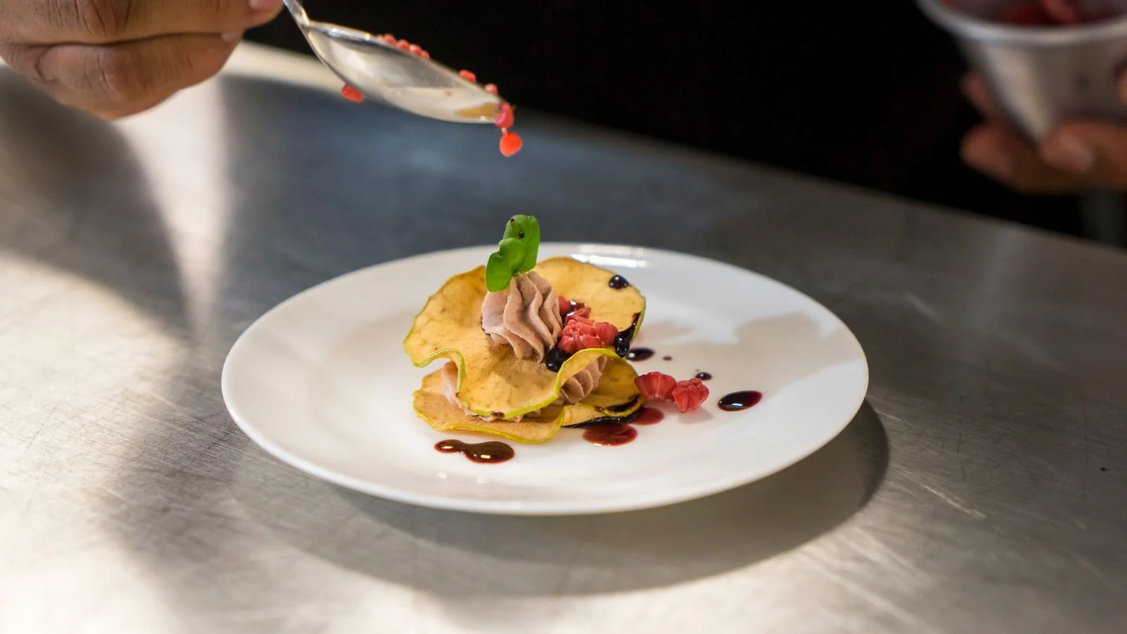 A chef garnishing an elegant dessert with berry sauce on a white plate