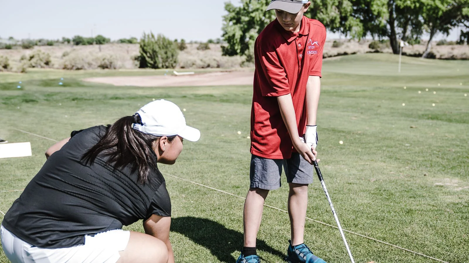 Golf instructor guiding a young golfer on a practice green on a sunny day