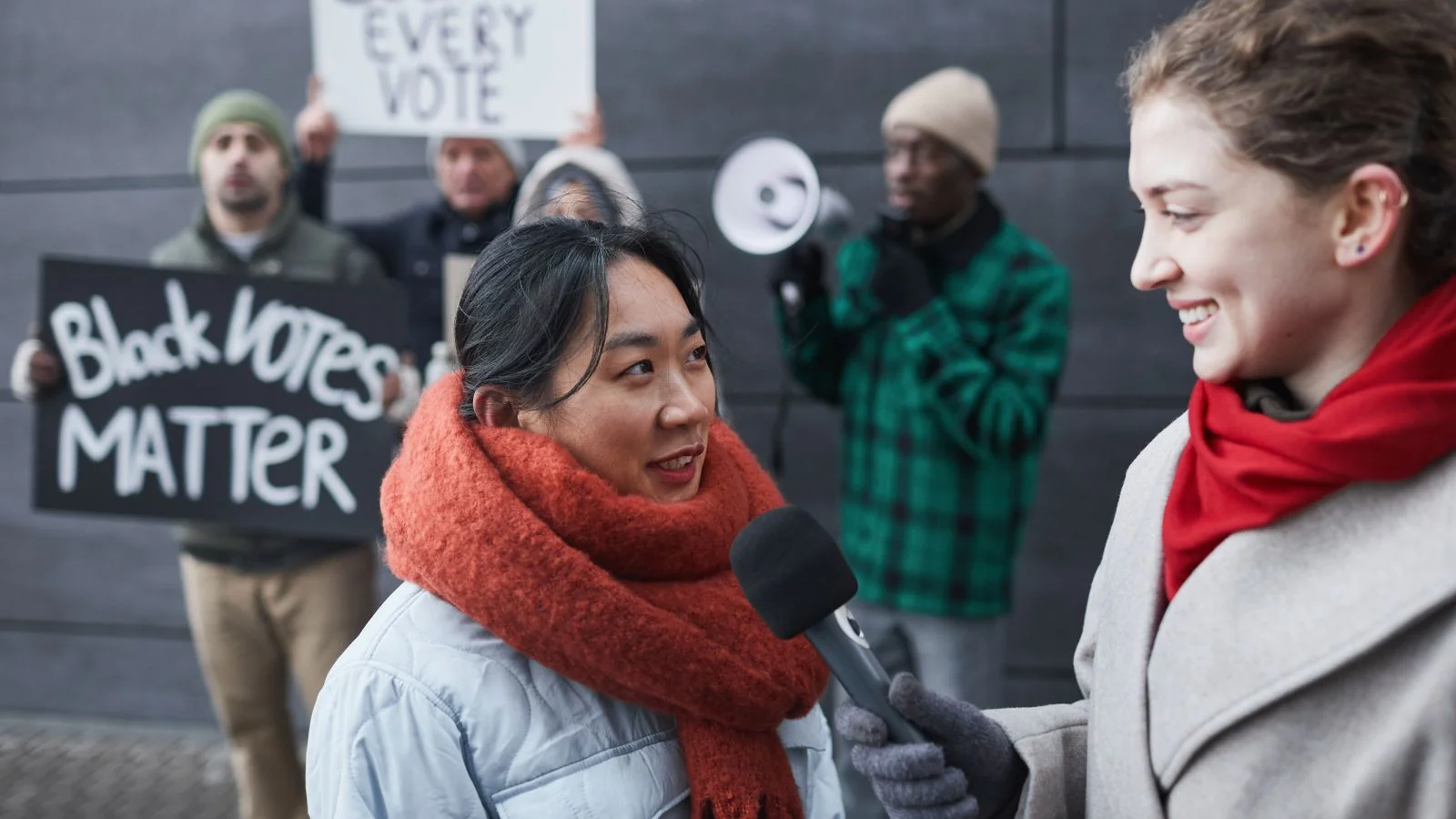A reporter interviewing a woman at a street demonstration, notebook in hand