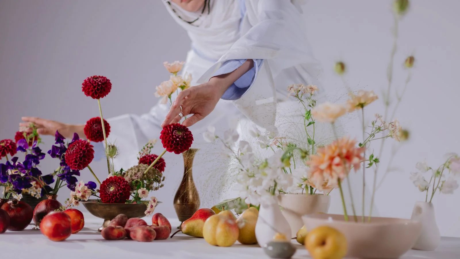 A woman in white arranging vibrant flowers and fruit on a table, the kind of styling a shelter-title submission needs before the shoot