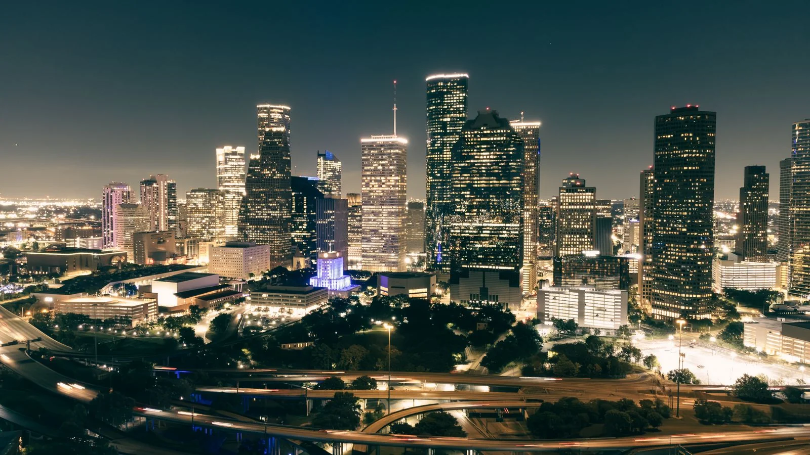 Aerial nighttime view of the Houston skyline lit up against a dark sky, the operational geography the Chronicle's beat reporters cover every day.
