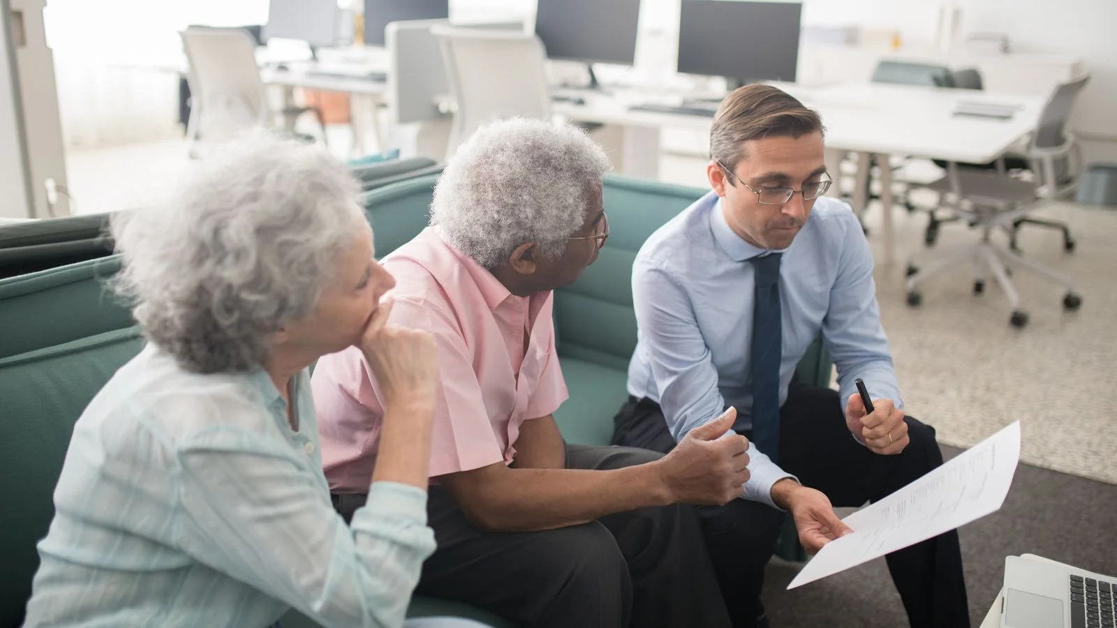 An advisor reviews paperwork with an older couple across an office desk, the client relationship InvestmentNews readers manage every day